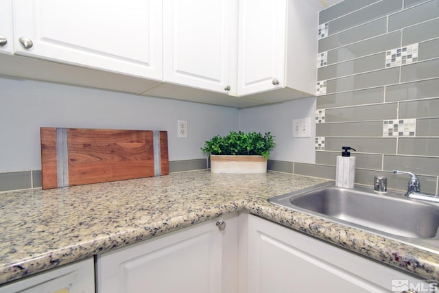 kitchen featuring light stone countertops, white cabinetry, and sink