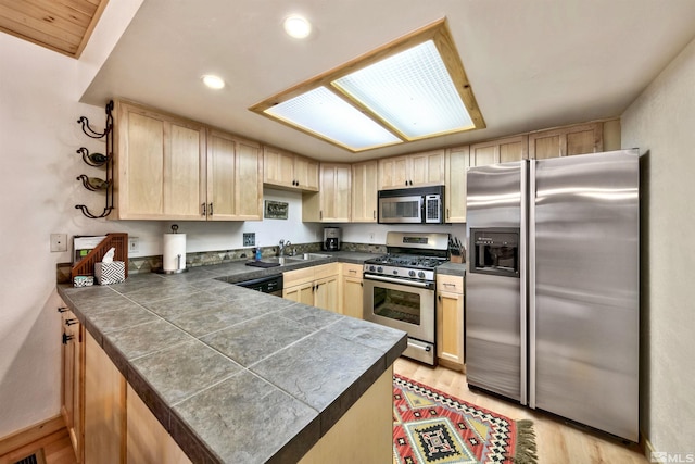 kitchen featuring light brown cabinetry, light hardwood / wood-style floors, stainless steel appliances, and kitchen peninsula