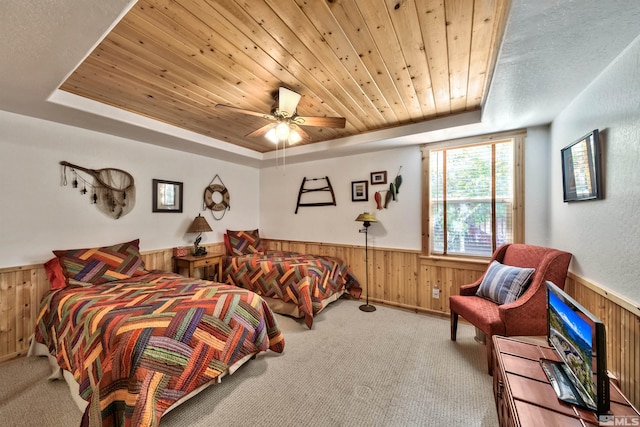 bedroom featuring ceiling fan, a tray ceiling, wood walls, and light colored carpet