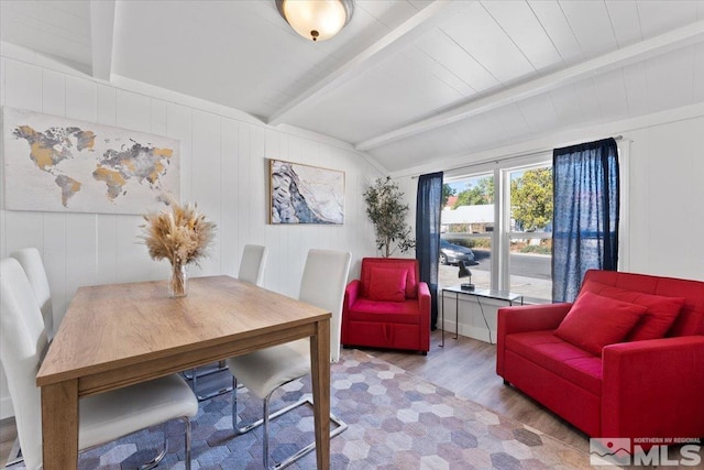 dining room featuring vaulted ceiling with beams, wooden walls, and light wood-type flooring