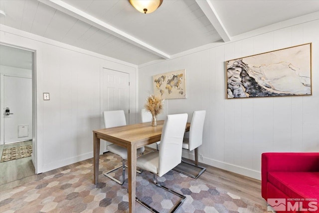 dining space featuring wooden walls, beam ceiling, and light wood-type flooring