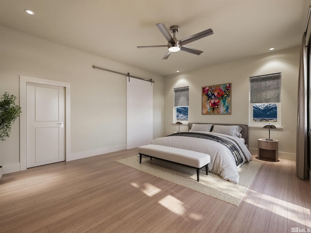 bedroom with a barn door, light hardwood / wood-style flooring, and ceiling fan