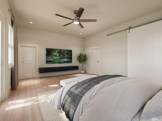 bedroom with a barn door, light hardwood / wood-style flooring, and ceiling fan