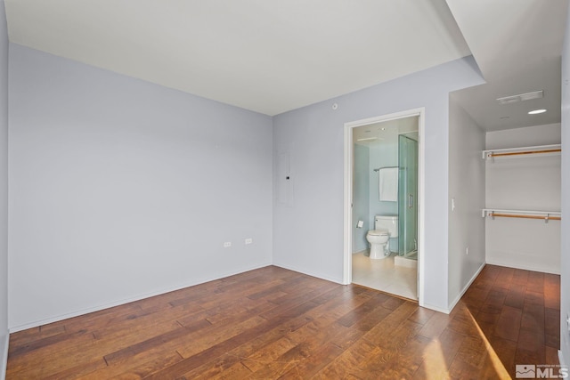 unfurnished bedroom with visible vents, baseboards, a closet, wood-type flooring, and a walk in closet