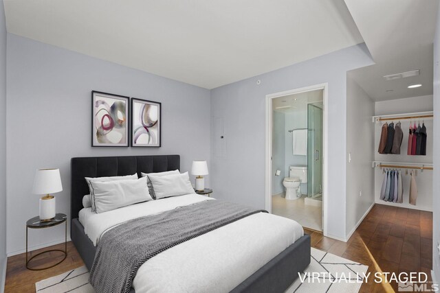 bedroom with wood finished floors, visible vents, baseboards, a closet, and ensuite bath