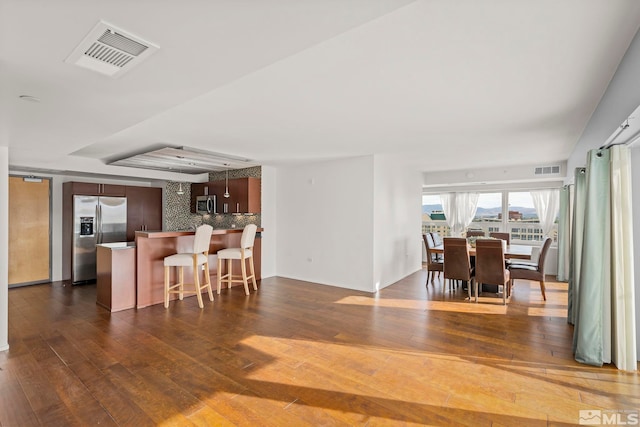 kitchen with kitchen peninsula, appliances with stainless steel finishes, backsplash, dark wood-type flooring, and a breakfast bar area