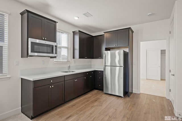 kitchen with appliances with stainless steel finishes, dark brown cabinetry, sink, and light hardwood / wood-style flooring