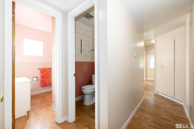 hallway with a healthy amount of sunlight, tile walls, and light hardwood / wood-style flooring