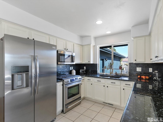 kitchen featuring decorative backsplash, stainless steel appliances, dark stone countertops, sink, and white cabinetry