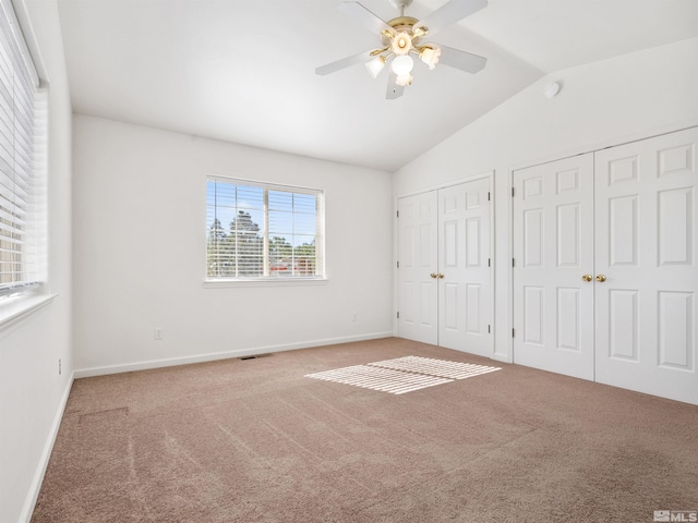 unfurnished bedroom featuring multiple closets, ceiling fan, carpet, and vaulted ceiling