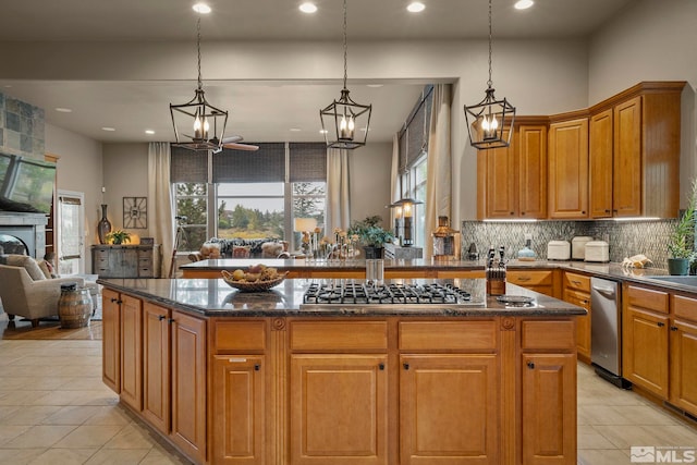 kitchen featuring decorative backsplash, a tiled fireplace, stainless steel gas stovetop, light tile patterned flooring, and decorative light fixtures