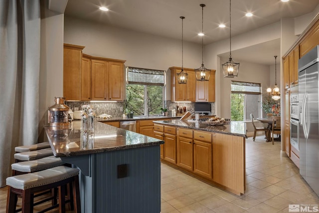 kitchen featuring a breakfast bar, dark stone countertops, stainless steel appliances, decorative light fixtures, and a center island