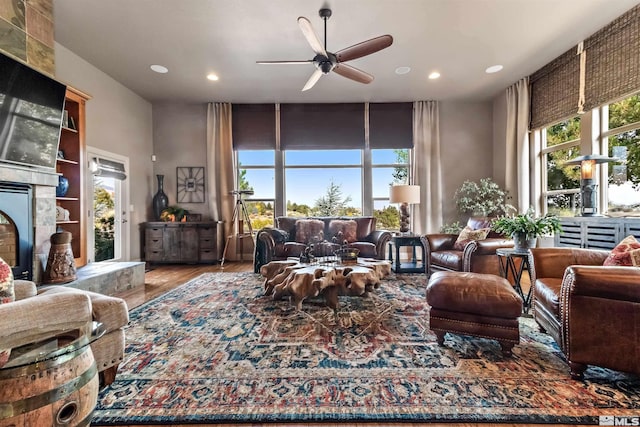 living room featuring built in shelves, hardwood / wood-style floors, a tiled fireplace, and ceiling fan