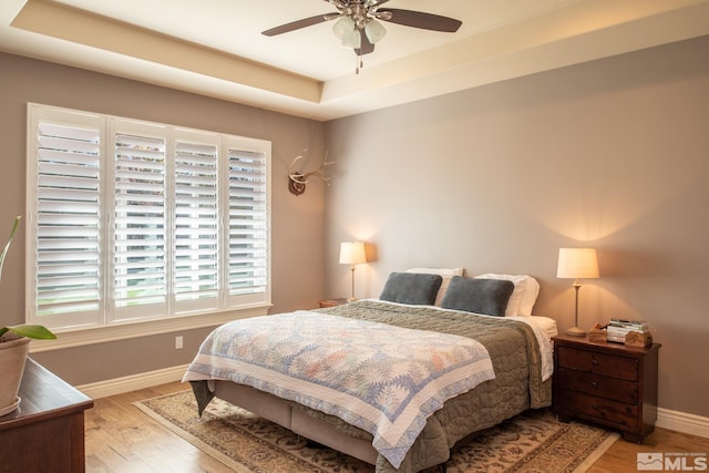 bedroom featuring ceiling fan, a tray ceiling, and light wood-type flooring