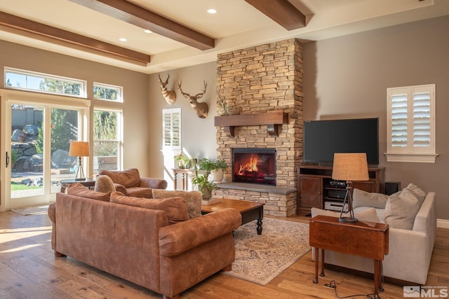 living room featuring beam ceiling, a stone fireplace, and light hardwood / wood-style flooring