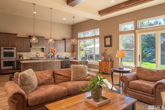 living room featuring beamed ceiling, sink, light hardwood / wood-style flooring, and a towering ceiling