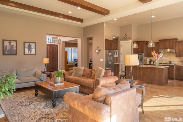 living room with beam ceiling, an inviting chandelier, a high ceiling, and light hardwood / wood-style floors