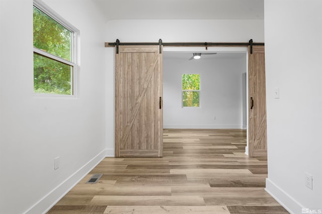 spare room featuring light hardwood / wood-style floors, a barn door, and a healthy amount of sunlight