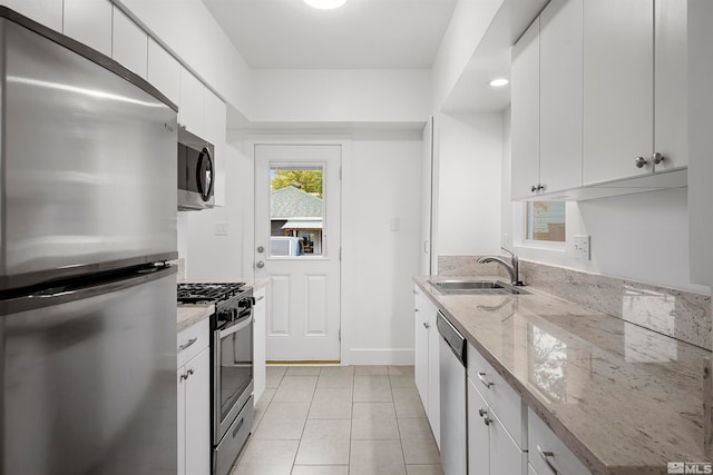 kitchen featuring sink, light tile patterned flooring, stainless steel appliances, white cabinets, and light stone counters