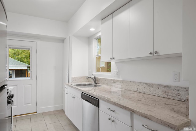 kitchen featuring sink, light stone countertops, light tile patterned floors, stainless steel dishwasher, and white cabinetry