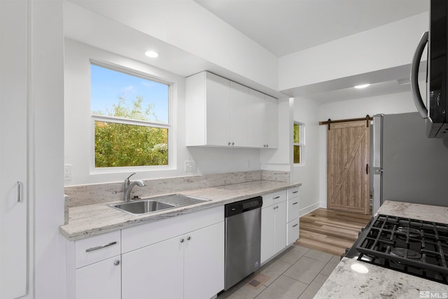 kitchen with white cabinets, a barn door, sink, light hardwood / wood-style floors, and stainless steel appliances