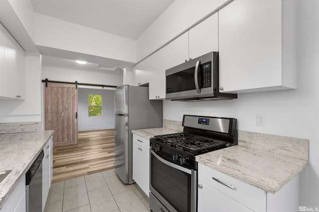 kitchen featuring light hardwood / wood-style floors, white cabinetry, a barn door, and stainless steel appliances