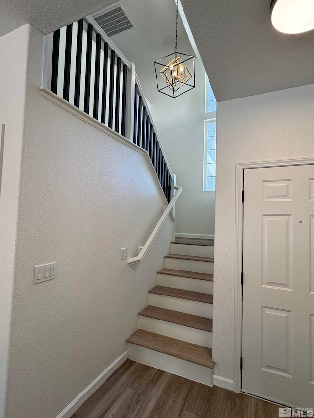 staircase with hardwood / wood-style floors and a chandelier