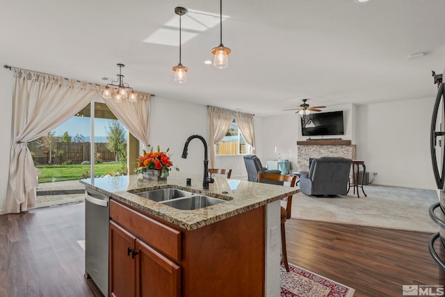 kitchen featuring a kitchen island with sink, dark hardwood / wood-style floors, pendant lighting, a stone fireplace, and sink