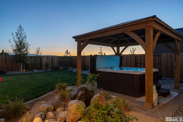 yard at dusk featuring a gazebo, a hot tub, and a patio area