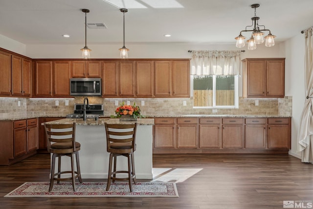 kitchen with a breakfast bar area, dark wood-type flooring, appliances with stainless steel finishes, and light stone countertops