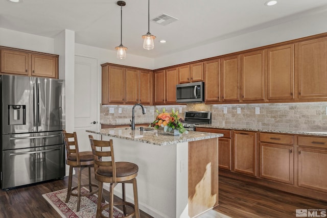 kitchen with dark hardwood / wood-style flooring, a kitchen island with sink, light stone countertops, sink, and stainless steel appliances