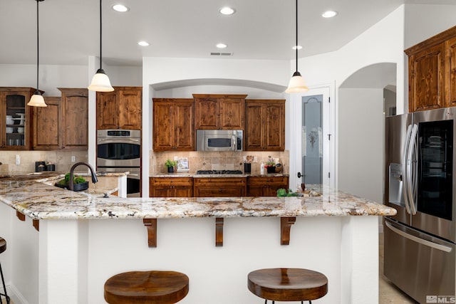 kitchen featuring appliances with stainless steel finishes, light stone countertops, decorative light fixtures, and a breakfast bar area