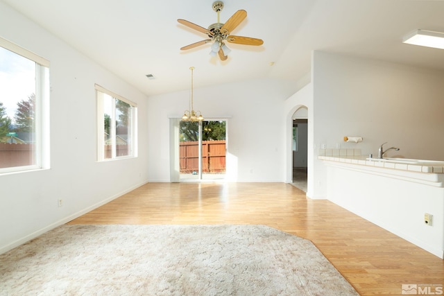 unfurnished living room featuring light hardwood / wood-style flooring, ceiling fan with notable chandelier, and vaulted ceiling