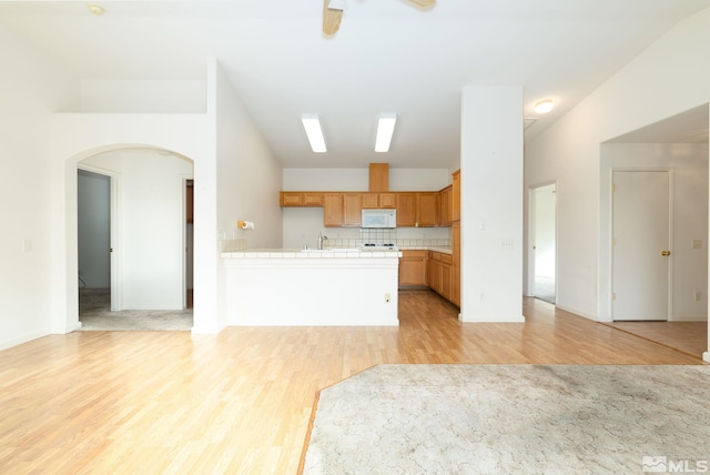 kitchen with tile countertops, sink, light hardwood / wood-style flooring, and backsplash