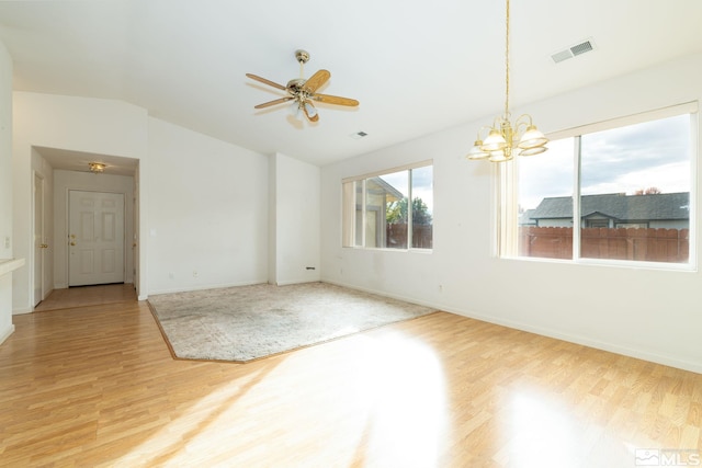 empty room with hardwood / wood-style flooring, vaulted ceiling, and ceiling fan with notable chandelier