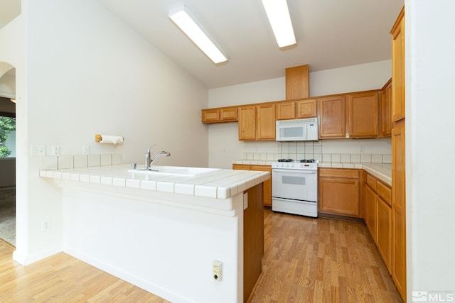 kitchen with tile counters, kitchen peninsula, light wood-type flooring, and white appliances