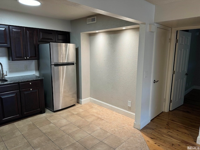 kitchen with decorative backsplash, dark brown cabinets, light wood-type flooring, and stainless steel refrigerator