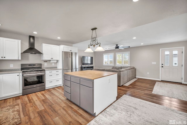 kitchen featuring wall chimney range hood, white cabinetry, light wood-type flooring, stainless steel appliances, and a center island