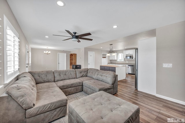 living room with light hardwood / wood-style flooring, ceiling fan with notable chandelier, and a wealth of natural light