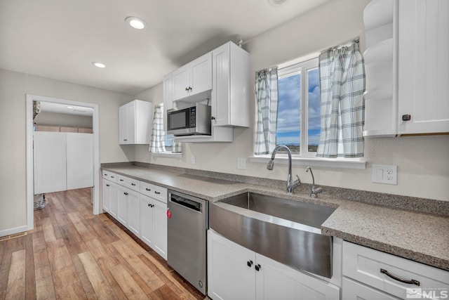 kitchen featuring sink, stainless steel appliances, white cabinets, light stone counters, and light hardwood / wood-style flooring