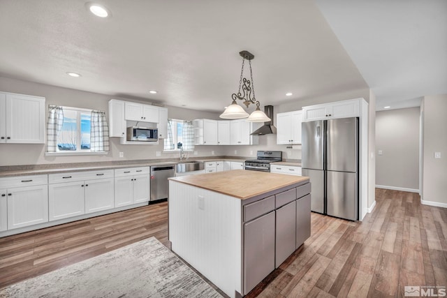 kitchen featuring a kitchen island, hanging light fixtures, stainless steel appliances, white cabinetry, and light hardwood / wood-style floors