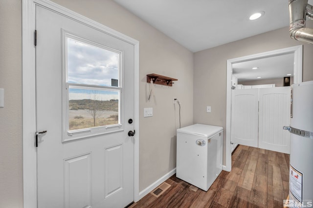 doorway to outside featuring dark wood-type flooring, a healthy amount of sunlight, and strapped water heater