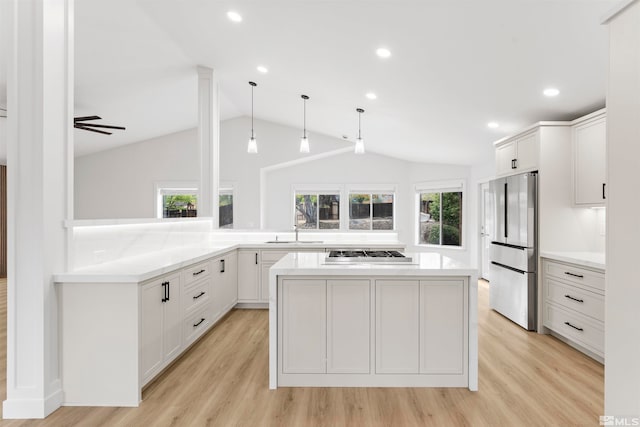 kitchen with light hardwood / wood-style floors, kitchen peninsula, appliances with stainless steel finishes, decorative light fixtures, and vaulted ceiling