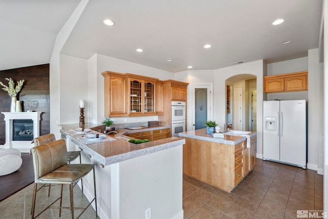 kitchen featuring lofted ceiling, kitchen peninsula, sink, a kitchen bar, and white appliances