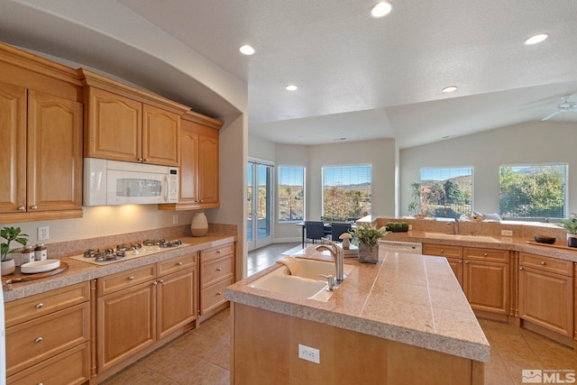 kitchen featuring white appliances, sink, vaulted ceiling, light tile patterned floors, and a center island with sink