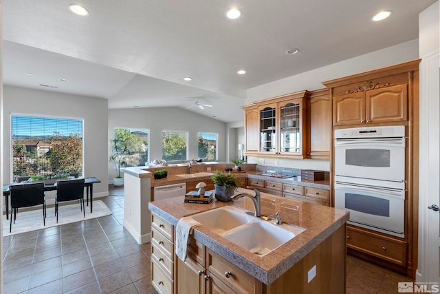 kitchen with dark tile patterned flooring, sink, double oven, lofted ceiling, and a center island with sink