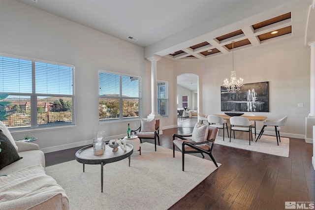 living room featuring decorative columns, coffered ceiling, dark wood-type flooring, beam ceiling, and an inviting chandelier