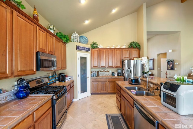 kitchen with tile countertops, sink, stainless steel appliances, and high vaulted ceiling