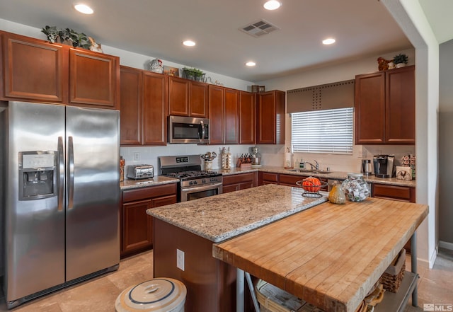 kitchen with light stone countertops, appliances with stainless steel finishes, sink, a kitchen bar, and a kitchen island