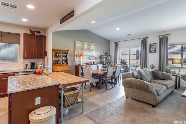 kitchen with light stone countertops, a kitchen island, backsplash, vaulted ceiling, and stainless steel dishwasher